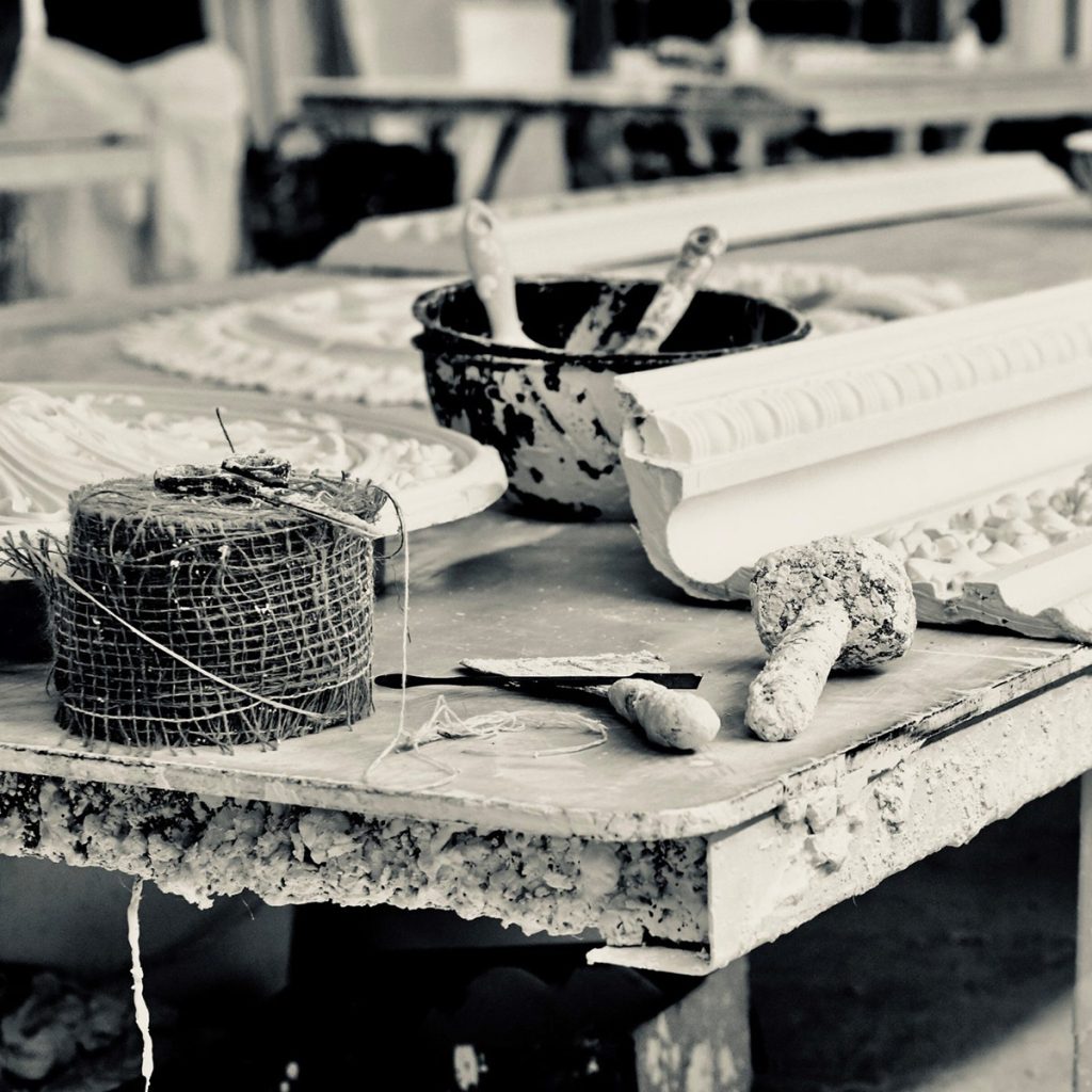 Plaster cornice being handcrafted on workshop bench with tools and mouldings