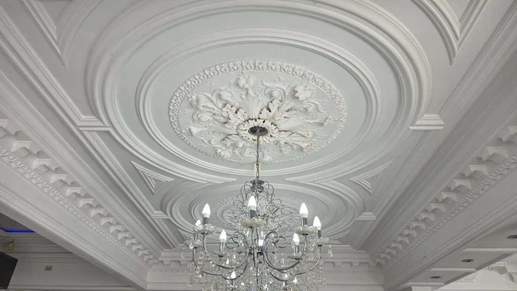 Bespoke plaster ceiling rose and decorative cornice installation with chandelier in finished interior