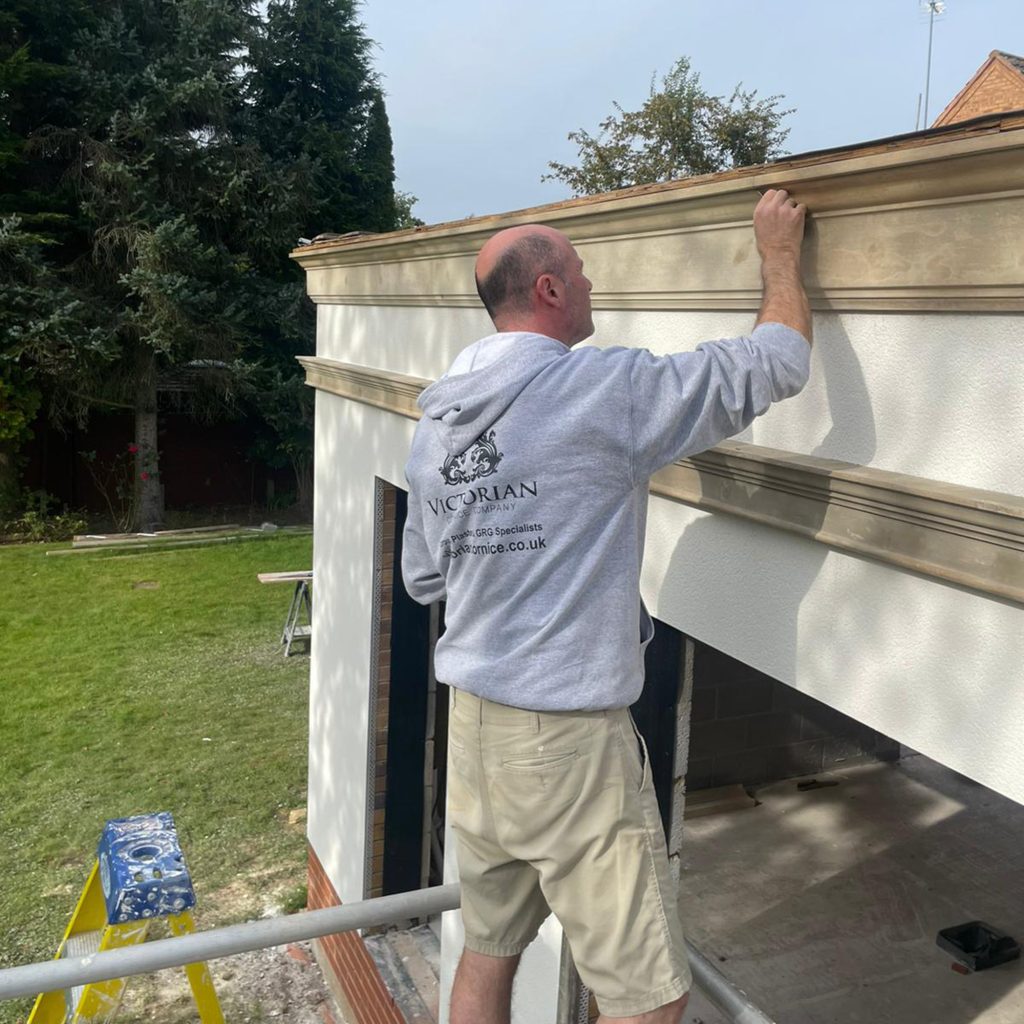 Skilled craftsman installing handmade exterior cornice on a residential property using traditional installation methods.