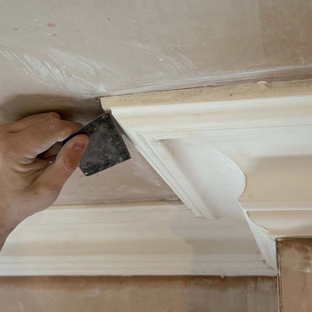 Craftsman hand finishing a plaster cornice joint during installation in Cobham